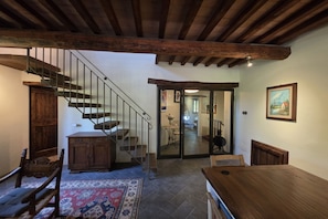 A spacious room with a wooden staircase, a dining table, and a view into another room. - Villa Tufi by MMega (Montone)
