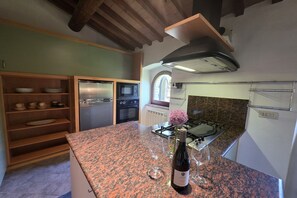 A kitchen with granite countertops, a stainless steel range hood, and a wine bottle on the counter. - Villa Tufi by MMega (Montone)