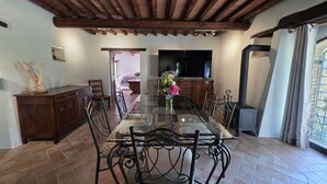 A dining area with a glass-top table, metal chairs, a wooden cabinet, and a television on the wall. - Villa Tufi by MMega (Montone)