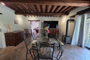 A dining area with a glass-top table, metal chairs, a wooden cabinet, and a television on the wall. - Villa Tufi by MMega (Montone)