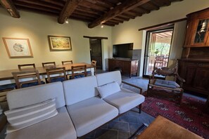 Uma sala de estar com um sofá, uma televisão e um espaço de refeições com cadeiras e uma mesa.