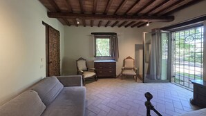 A room with a wooden ceiling, a sofa, a chair, a small table, and a window with curtains. - Villa Tufi by MMega (Montone)