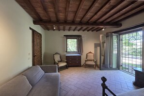 A room with a wooden ceiling, a sofa, a chair, a small table, and a window with curtains. - Villa Tufi by MMega (Montone)
