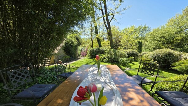 A wooden table set with a white tablecloth, surrounded by chairs, in a lush garden with trees and shrubs. - Villa Tufi by MMega (Montone)