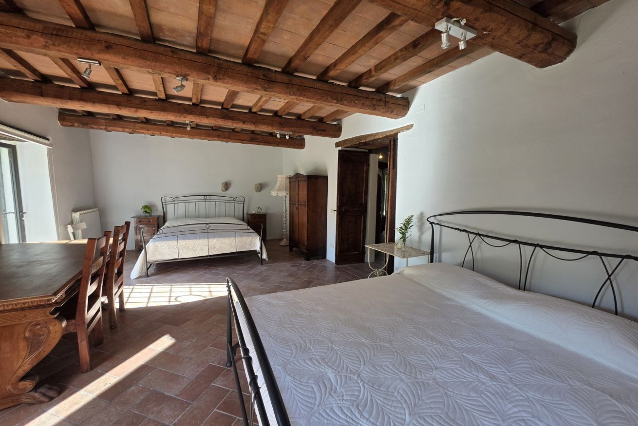 Une chambre avec un grand lit, une table à manger en bois et une chaise. Une fenêtre laisse entrer la lumière naturelle.
