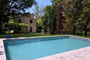 A rectangular swimming pool with a stone border, surrounded by a well-maintained lawn and a stone building with a window. - Villa Tufi by MMega (Montone)