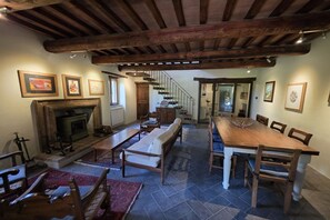 A spacious living room with a fireplace, a dining table, and a staircase leading to another level. - Villa Tufi by MMega (Montone)