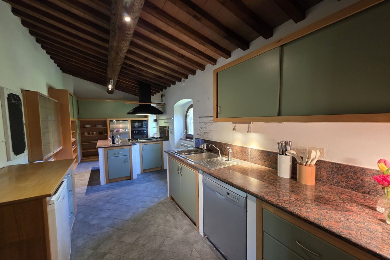 A kitchen with a central island, wooden ceiling beams, and a view into the dining area.