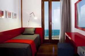 Ein Schlafzimmer mit Bett, Schreibtisch, Stuhl, einem Fenster mit Meerblick und einer Tür.