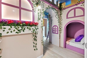Ein Kinderzimmer mit Fenster, einem Bett und einer an der Wand befestigten Regal mit Blumen.
