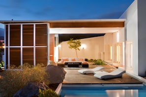 A modern outdoor pool area with a wooden deck, lounge chairs, and a seating area with cushions. - Casas Bioclimáticas Iter El Rio (Granadilla de Abona)