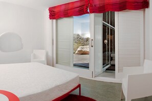 A bedroom with a bed, a window with a view, and a door leading to an outdoor area. - Casas Bioclimáticas Iter El Rio (Granadilla de Abona)