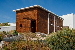 A modern building with a wooden facade, a circular window, and a flat roof. - Casas Bioclimáticas Iter El Rio (Granadilla de Abona)
