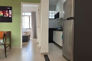 Une cuisine moderne avec un réfrigérateur en acier inoxydable, un coin repas avec une chaise en bois et une vue sur l’extérieur par une porte.