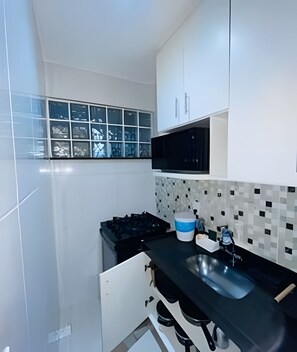 Une cuisine de taille réduite avec des meubles blancs, un plan de travail noir et un revêtement mural en carreaux.