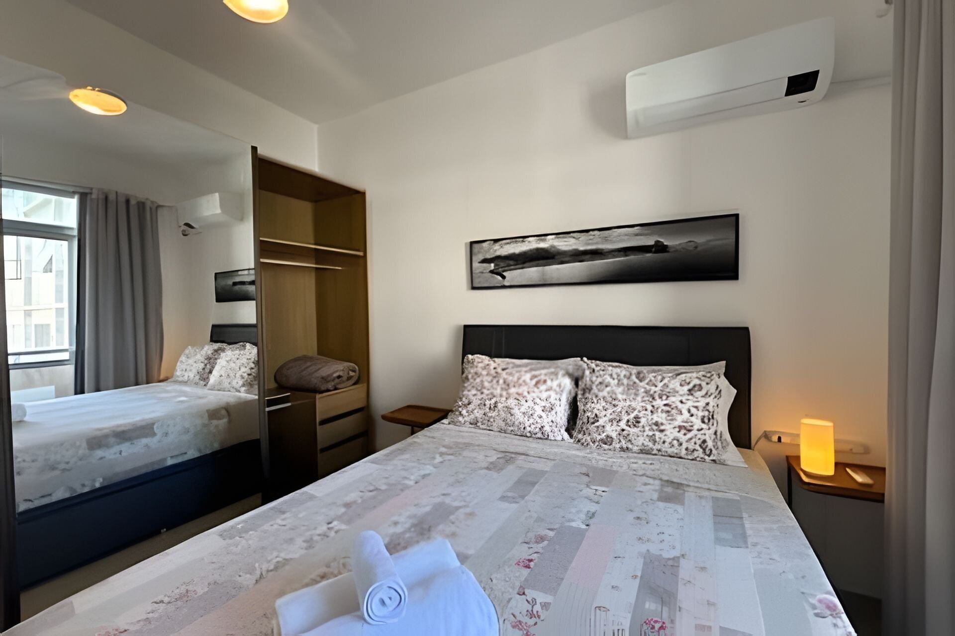 Une chambre d’hôtel équipée d’un lit, d’une armoire, d’une table de chevet, d’une lampe et d’un climatiseur fixé au mur.
