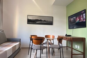 Ein modernes Zimmer mit einer Couch, einem Esstisch mit Stühlen, einem an der Wand befestigten Flachbildfernseher und einem gerahmten Landschaftsfoto.
