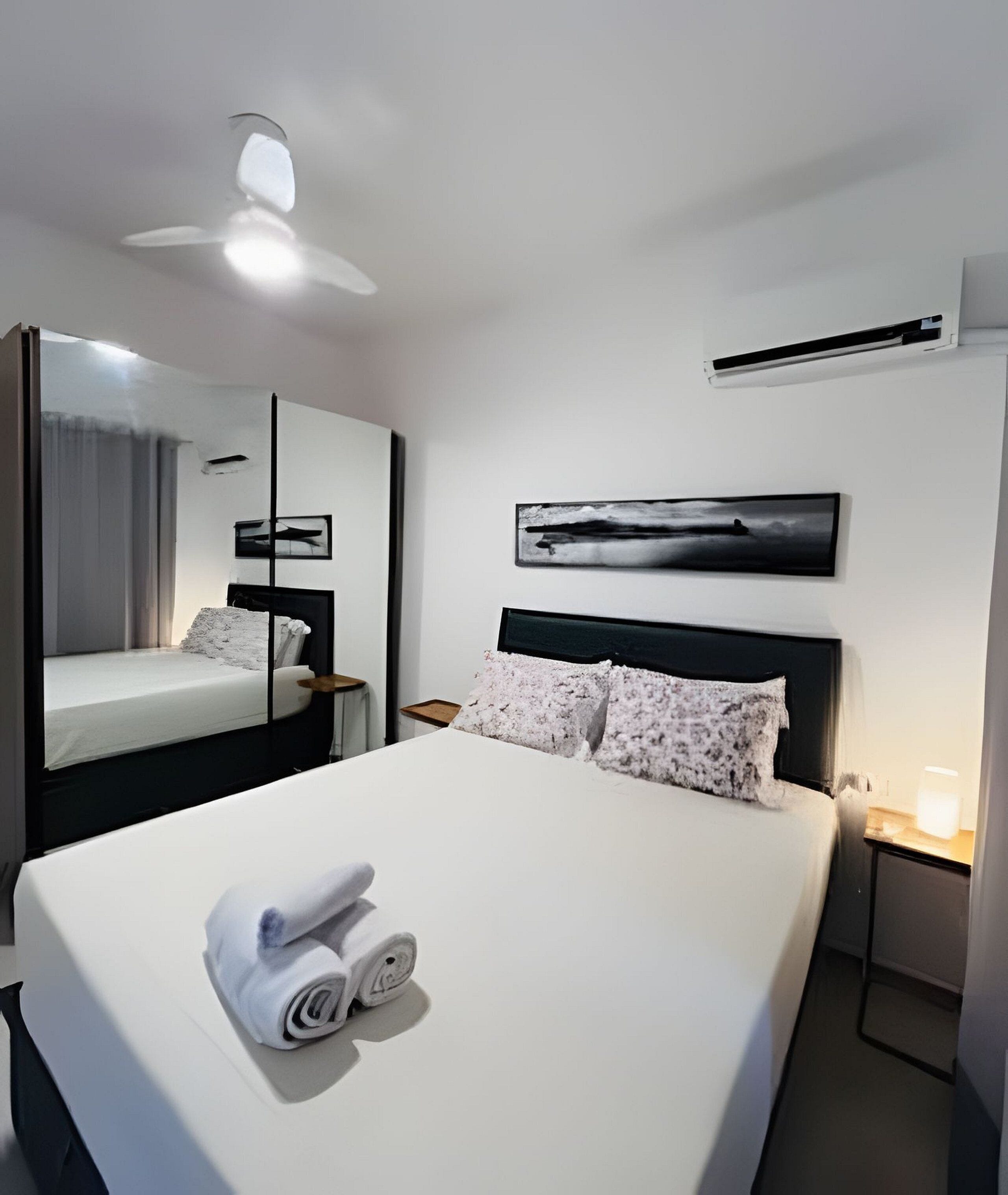 Une chambre d’hôtel avec un grand lit, un ventilateur de plafond, un appareil de climatisation, une table de chevet avec une lampe et un tableau encadré au mur.