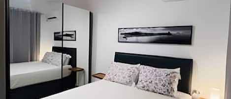 A hotel room with a large bed, a ceiling fan, an air conditioning unit, a bedside table with a lamp, and a framed picture on the wall.