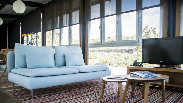 A modern living room with a light blue sofa, a flat-screen TV, and a patterned rug. - Casas Bioclimáticas Iter La Religa (Granadilla de Abona)