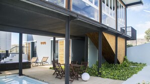 A modern outdoor pool area with a wooden deck, lounge chairs, and a table. - Casas Bioclimáticas Iter La Religa (Granadilla de Abona)