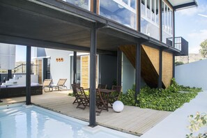 Ein Poolbereich im Freien mit modernem Design, einer Holzterrasse, Liegestühlen und einem Tisch.