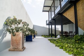 Un'area esterna moderna con piante in vaso, un angolo relax con sedie e un edificio con ampie finestre.
