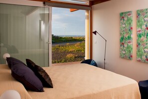 A bedroom with a bed, a chair, a floor lamp, and a view of the outdoors. - Casas Bioclimáticas Iter El Escudo (Granadilla de Abona)
