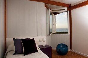 A bedroom with a bed, pillows, a nightstand, a lamp, a window with a view of the sea, and a blue exercise ball. - Casas Bioclimáticas Iter El Escudo (Granadilla de Abona)