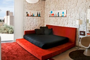 A modern bedroom with a red sofa bed, a large window, and artwork on the walls. - Casas Bioclimáticas Iter El Bernegal (Granadilla de Abona)