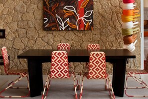 A dining area with a stone wall, a dark wooden table, and patterned chairs. - Casas Bioclimáticas Iter El Bernegal (Granadilla de Abona)