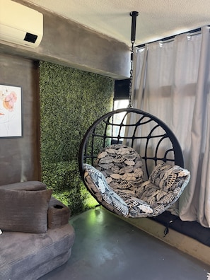 A room with a hanging chair, a sofa, a wall-mounted air conditioner, and a green wall. - Style & Comfort - SampaSky (São Paulo)