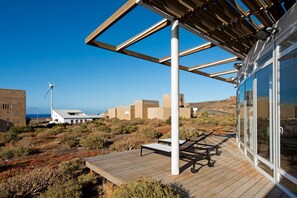 A wooden deck with a glass enclosure, a wind turbine, and buildings in the background. - Casas Bioclimáticas Iter La Vela (Granadilla de Abona)