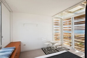 Quarto com uma cama, uma cadeira, uma mesinha e uma janela com persianas.
