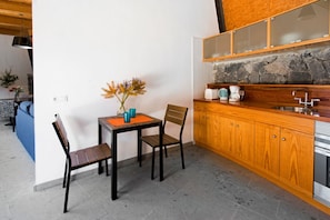 A compact kitchen with a stone backsplash, wooden cabinets, and a dining area with a table and chairs. - Casas Bioclimáticas Iter Noche y Dia (Granadilla de Abona)