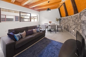 Een moderne woonkamer met een bank, een eettafel en stoelen. Er is een stenen muur en een raam met uitzicht.