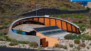 A modern building with a curved roof, solar panels, and a natural landscape in the background. - Casas Bioclimáticas Iter Noche y Dia (Granadilla de Abona)