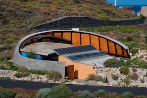 A modern building with a curved roof, solar panels, and a natural landscape in the background. - Casas Bioclimáticas Iter Noche y Dia (Granadilla de Abona)