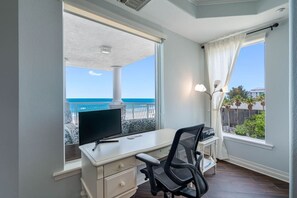 A room with a desk, chair, and a large window offering a view of the ocean. - Luxury Beach Front at Fairwinds 402 (Indian Shores)