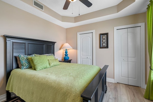 Quarto com cama, mesa de cabeceira, ventilador de teto e duas portas.