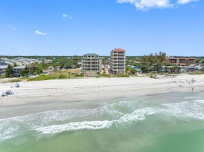 Ein Strandhotel mit mehreren Gebäuden, einem Sandstrand und Meereswellen.