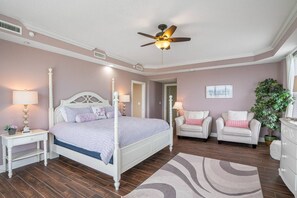 A bedroom with a four-poster bed, two bedside tables, a ceiling fan, a large potted plant, and a view of the hallway. - Luxury Beach Front at Fairwinds 402 (Indian Shores)