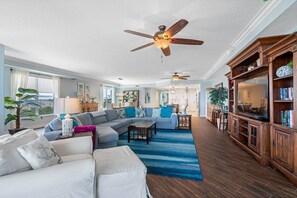 A spacious living room with a sectional sofa, a dining area, and a wooden entertainment center. - Luxury Beach Front at Fairwinds 402 (Indian Shores)