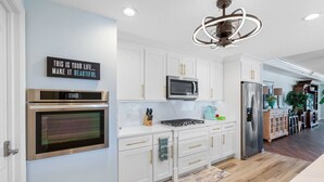 Una cocina moderna con armarios blancos, electrodomésticos de acero inoxidable y un letrero decorativo en la pared.