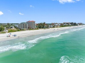 Uma praia com vista clara para o oceano, areal arenoso e edifícios ao fundo.