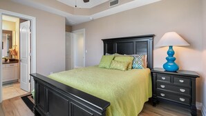 Un dormitorio con cama, mesita de noche, lámpara, ventilador de techo y puerta que da al baño.