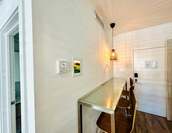 Une pièce moderne avec une table en verre, des chaises en bois, un climatiseur fixé au mur et un luminaire suspendu.