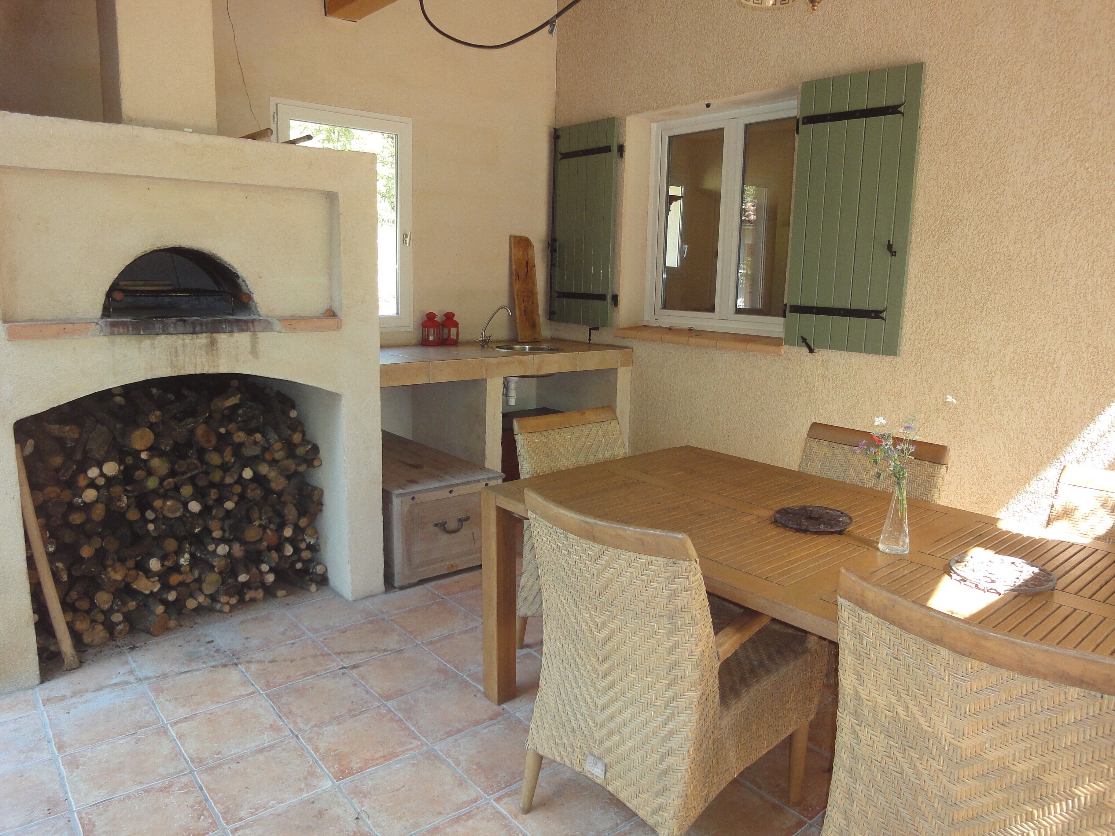 Une cuisine rustique avec un poêle à bois, une table à manger entourée de chaises en osier et une fenêtre avec des volets.