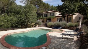 A pool area with a stone patio, lounge chairs, and a building in the background. - Holiday Home “Waterballet” with Pizza Oven, Wifi, and Air Conditioning (Villecroze)