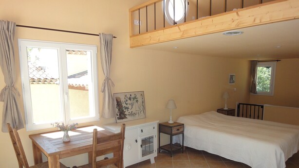 A bedroom with a bed, a desk, and a chair. There is a window with curtains, a painting on the wall, and a lamp on a bedside table. - Holiday Home “Waterballet” with Pizza Oven, Wifi, and Air Conditioning (Villecroze)